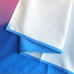 A large table runner featuring a gradient design with shades of blue and white. It has a stitched edge and branding.