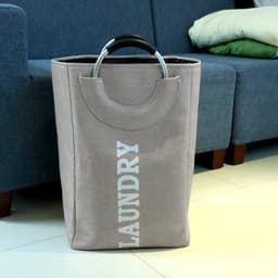 A beige laundry basket with a handle and the word "LAUNDRY" printed on the front, placed beside a couch.