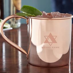 A copper Moscow Mule mug with a handle, filled with ice and garnished with lime and mint, featuring a logo.