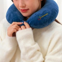 A U-shaped travel pillow in blue fabric, featuring a logo, held by a person wearing a white sweater.