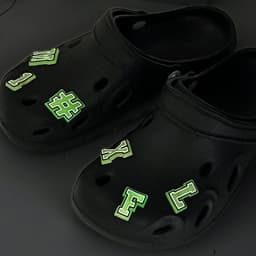 Black clog shoes adorned with green glowing charm letters and symbols for a fun and novelty look.