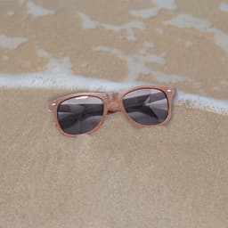 Coffee fibre sunglasses in a brown hue resting on sandy beach, with gentle waves in the background.