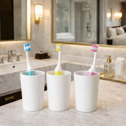 A set of three toothbrushes with blue, yellow, and pink heads in white cups on a marble bathroom counter.