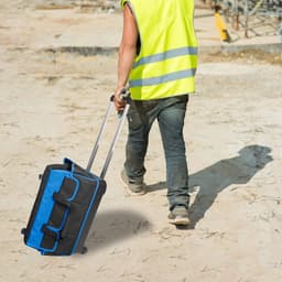 A wheeled tool bag in black and blue is being pulled along by a person in a high-visibility vest at a construction site.