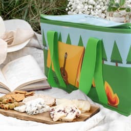 A green Sublimation Handle Cooler Bag with a campsite design, accompanied by a spread of cheese, crackers, and olives.