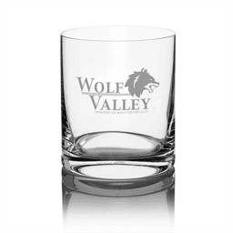 A clear glass whisky tumbler featuring a logo and a sturdy base. The glass has a polished finish.