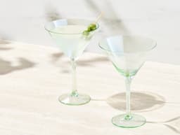 A set of two clear glass glamour martini glasses with green accents, featuring a cocktail garnished with an olive.