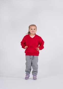 A girl wearing a red v-neck fleece jumper and grey track pants, smiling and standing against a plain background.