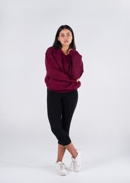 A unisex burgundy V-neck fleece jumper worn with black leggings and white sneakers, featuring a logo.