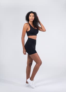 A model wearing black high rise legging shorts paired with a matching crop top and white sneakers, against a plain background.