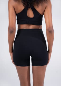 Black high-rise legging shorts featured on a model from the back, paired with a matching sports bra.