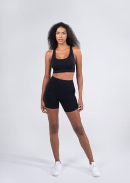 High rise legging shorts in black on a model, paired with a matching black crop top. The outfit features a logo.