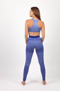 A model in blue seamless leggings and a matching sports bra, seen from the back. The outfit features a logo.