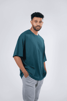 A unisex oversize easyfit tee in teal worn with grey sweatpants, featuring a logo on the tee.