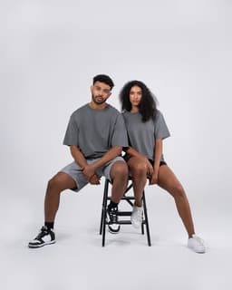 A unisex oversize easyfit tee in grey, worn by a male model seated and a female model on a stool.
