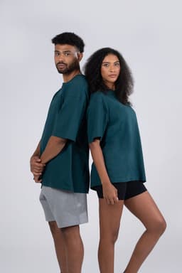 Two models wear unisex oversize easy-fit tees in a deep teal colour, standing back-to-back.