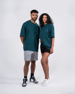 A teal oversized unisex T-shirt displayed on a male and female model, with a logo visible on the shirt.