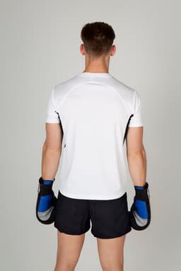 A man wearing a white cool dry T-shirt and black shorts, holding boxing gloves, viewed from the back.