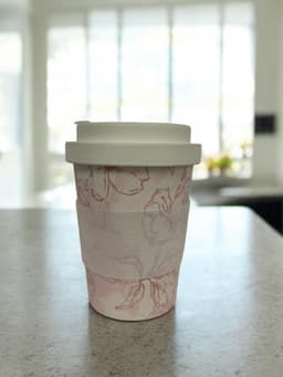 A reusable bamboo coffee cup with a hard lid, featuring a floral design in pink and white.