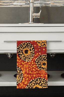 A multi-purpose towel in red, orange, yellow, and black patterns hanging from a kitchen towel rack.