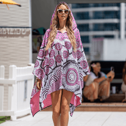 A vibrant pink and black patterned poncho with a hood, featuring circular designs. It has a logo on the front.