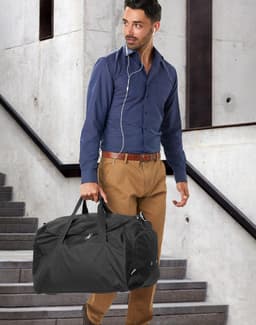 A red duffle bag with a zippered compartment and a pair of shoes resting against it. The bag has a logo.