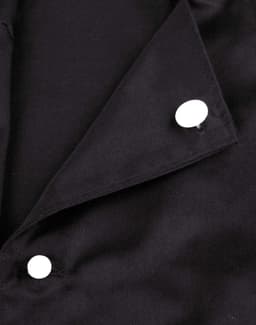 A close-up of a black chef jacket featuring two white exchangeable buttons on the collar.