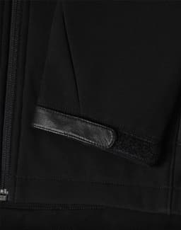 A black softshell jacket featuring a zippered front and a textured patch on the sleeve. It has a logo.