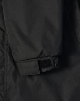 A close-up of a black long line stadium jacket featuring adjustable wrist cuffs and a logo.