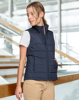 A navy insulated puffer vest with a 3D cut, featuring a zip front and side pockets, displayed on a model indoors.