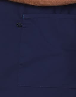 A navy scrub top featuring a large pocket and contrast brown collar. Includes a logo.