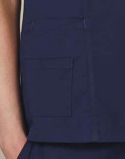 A deep navy scrub top featuring a pocket detail and contrast stitching. Includes a small logo on the garment.