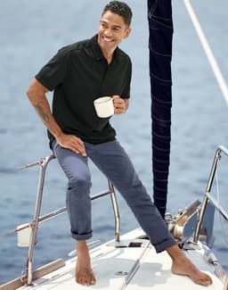 Men's flexi chino pants in navy, modelled by a man on a boat, wearing a black polo and holding a cup.