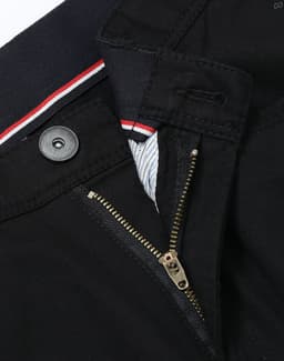 A close-up of black chino pants featuring a zip fly and button closure, with a striped waistband detail.