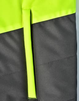 A hi-vis quilted safety jacket featuring a bright yellow upper and dark grey lower section, with a hanger loop.