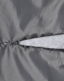 A close-up of a grey quilted fabric featuring a zippered section and a soft, light grey lining.