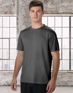 A men's short sleeve tee in grey, featuring a minimal design and a logo. The model stands against a large window background.