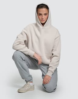 A unisex premium fleece oversized hoodie in light grey, worn by a model with grey tracksuit bottoms and sneakers.