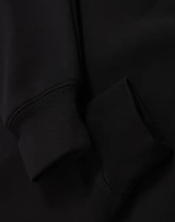 A black unisex premium fleece oversized hoodie with ribbed cuffs. The fabric appears soft and cozy.