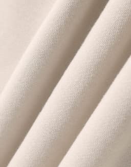A close-up of soft, beige fabric showcasing the texture of an oversized fleece hoodie. It includes a logo.