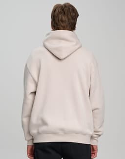A unisex premium fleece oversized hoodie in a light beige colour, featuring a hood and a branding logo on the back.