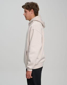 A unisex premium fleece oversized hoodie in light beige, featuring a hood and a front pocket, with a logo visible.