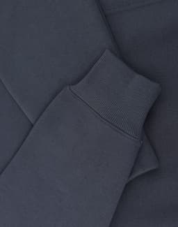 A close-up of a navy oversized hoodie featuring ribbed cuffs and soft fleece material. It includes a logo.