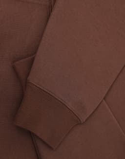 A brown unisex premium fleece oversized hoodie with ribbed cuffs and a soft finish. It features a logo.