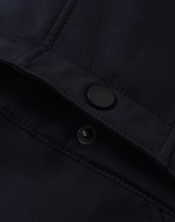 A close-up of a navy softshell jacket featuring a snap button and interior stitching details.