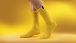 Bright yellow bamboo workwear socks displayed on a model's feet against a yellow background. The socks feature a logo.