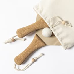Two cork beach rackets and a white ball, packaged in a cream drawstring bag.