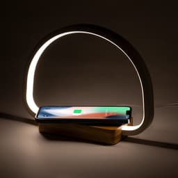A wireless charger lamp with a wooden base and a glowing white arch, holding a smartphone.