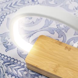A wireless charger lamp with a bamboo base and a glowing white light on a patterned surface.