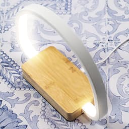 A wireless charger lamp with a white arch and a bamboo base, set against a decorative blue tile background.